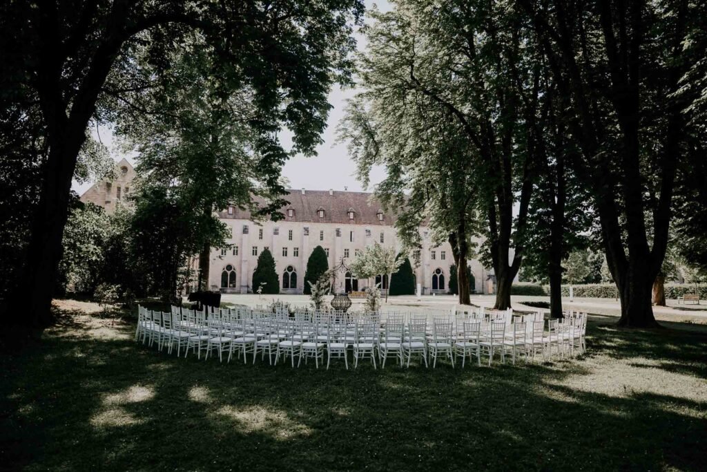 Cérémonie de mariage en plein air dans le parc verdoyant de l'Abbaye de Royaumont, entourée d'arbres majestueux et d'une architecture historique en arrière-plan