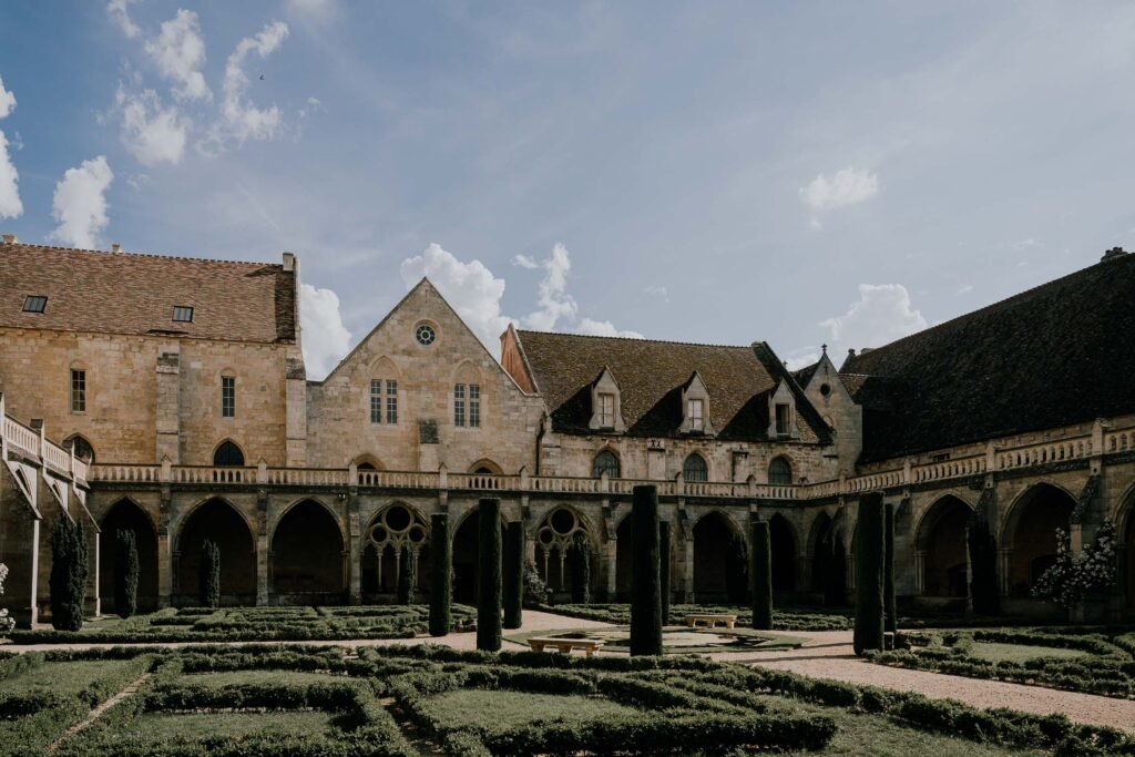 Perspective du cloître de l'Abbaye de Royaumont avec ses haies impeccables et son architecture historique baignée de lumière naturelle.