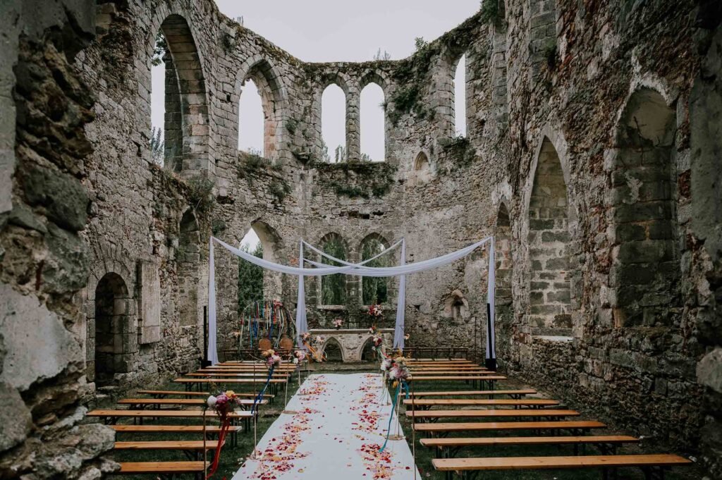 Cérémonie de mariage en plein air au cœur des ruines du Château de Vivier, avec une décoration romantique et des arches en pierre majestueuses.