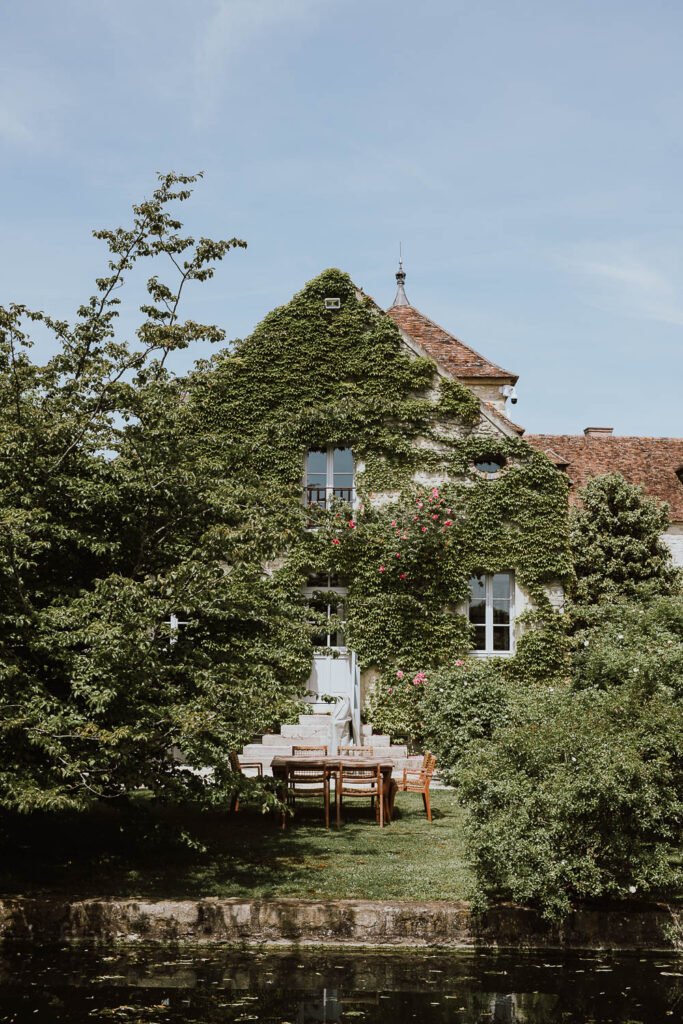 Vue du jardin luxuriant du Château de Berville, entouré de bâtiments en pierre recouverts de végétation, parfait pour un mariage romantique en Île-de-France