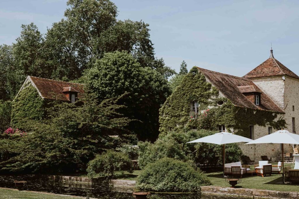 Façade recouverte de lierre du Château de Berville, avec une table extérieure installée près de l'eau pour un cadre enchanteur en Île-de-France