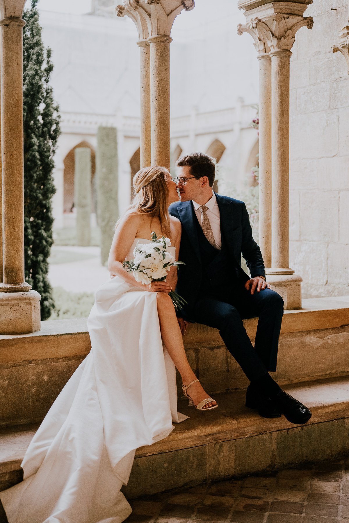 Bride and groom kissing under stone arches during a château wedding in France.